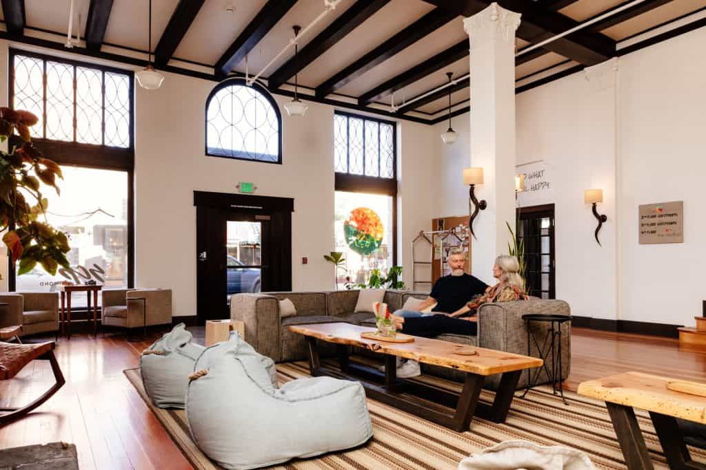 Two people sit on a couch in the lobby of SCP Redmond Hotel in Central Oregon