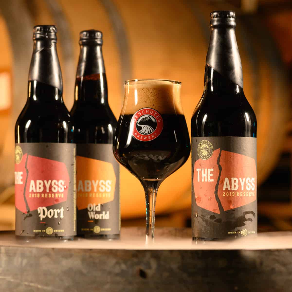 Three bottles of Deschutes Brewery Abyss reserve beer with a glass snifter of beer.