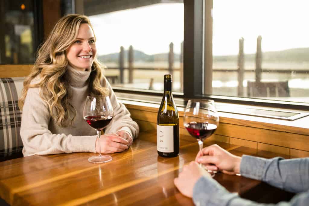 SRR_WinterLifestyle_03.22.21_TylerRoemer_ARR-083_HiRes a couple enjoying a glass of red wine in a booth at Carson’s with views of Mt Bachelor