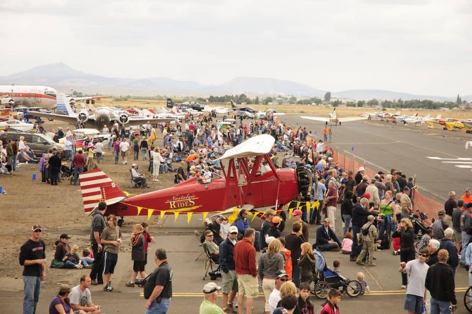 A crowd of people gather around vintage airplanes during the Airshow of the Cascades in Madras, Oregon.