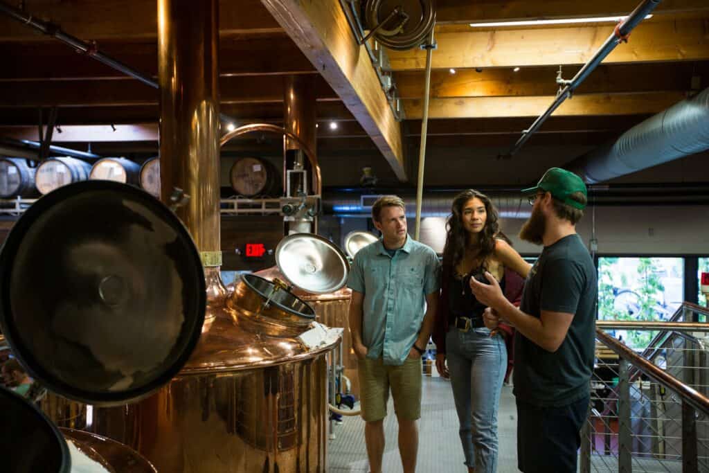 outdoor-adventure-travel-photography-by-steve-heinrichs_-70-large a couple talking to a brewmaster indoors next to shiny copper brew barrels