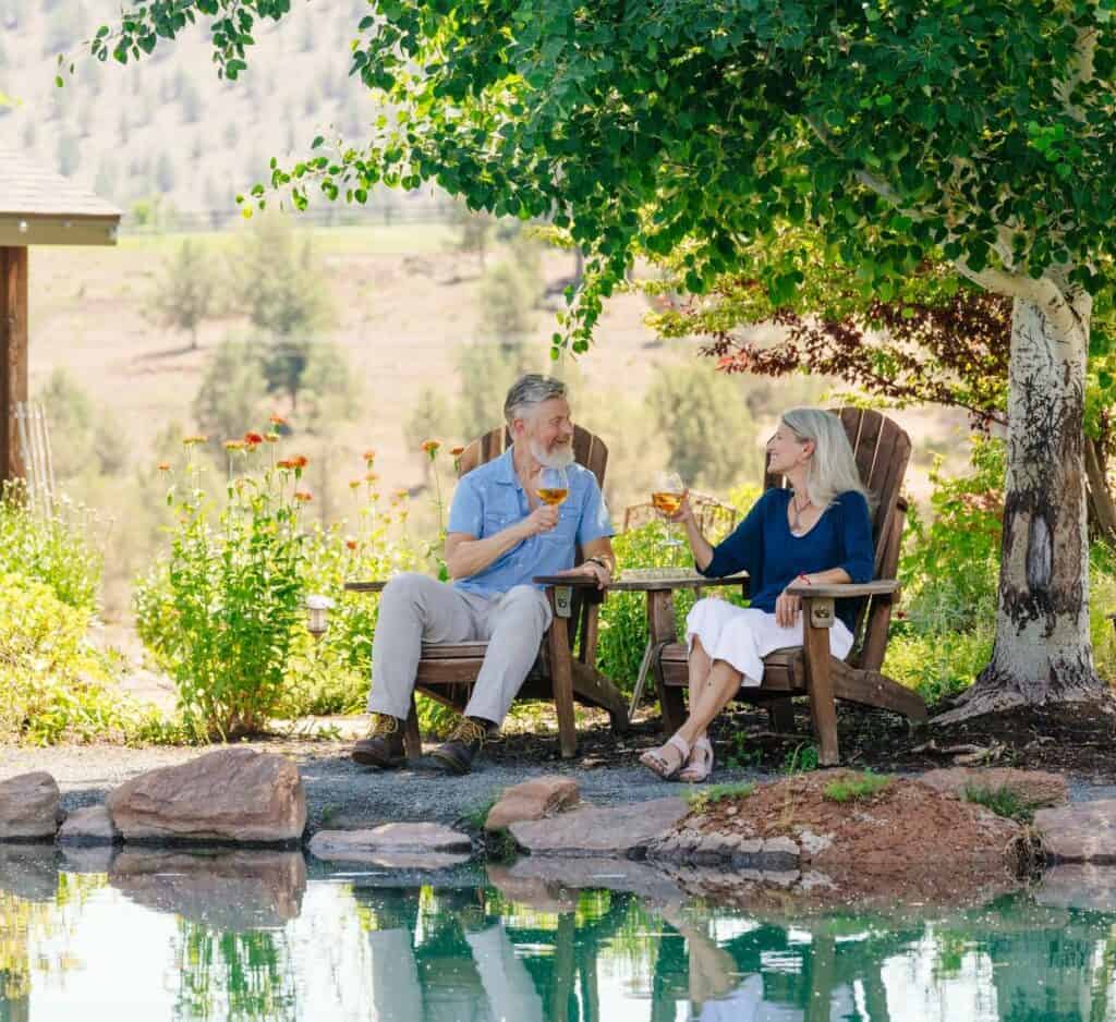 Faith Hope Charity Vineyards 2-large (3) a couple relaxing in adirondack chairs on the pond, enjoying a glass of wine at Faith, Hope and Charity Vineyards