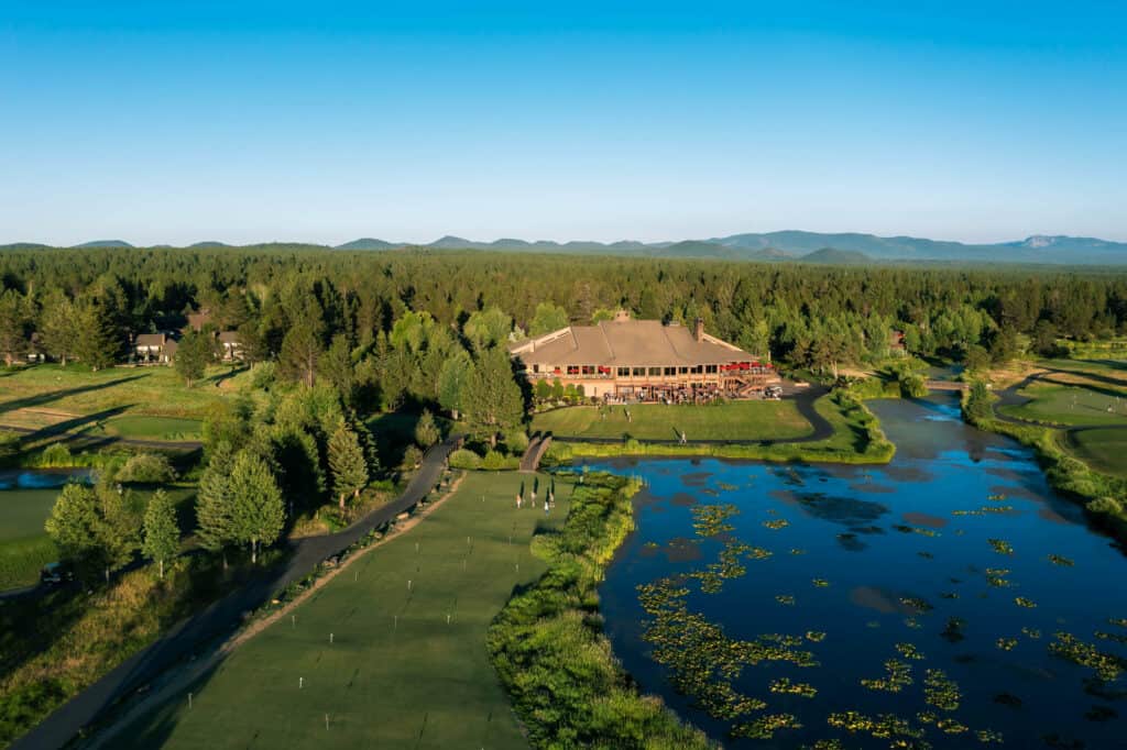 SRR_Mike West_ARR_Summer 2021_Lodge + Accommodations Exteriors-18 copy an ariel of the 2-story lodge at Sunriver Resort next to the river surrounded by forest and mountain peaks