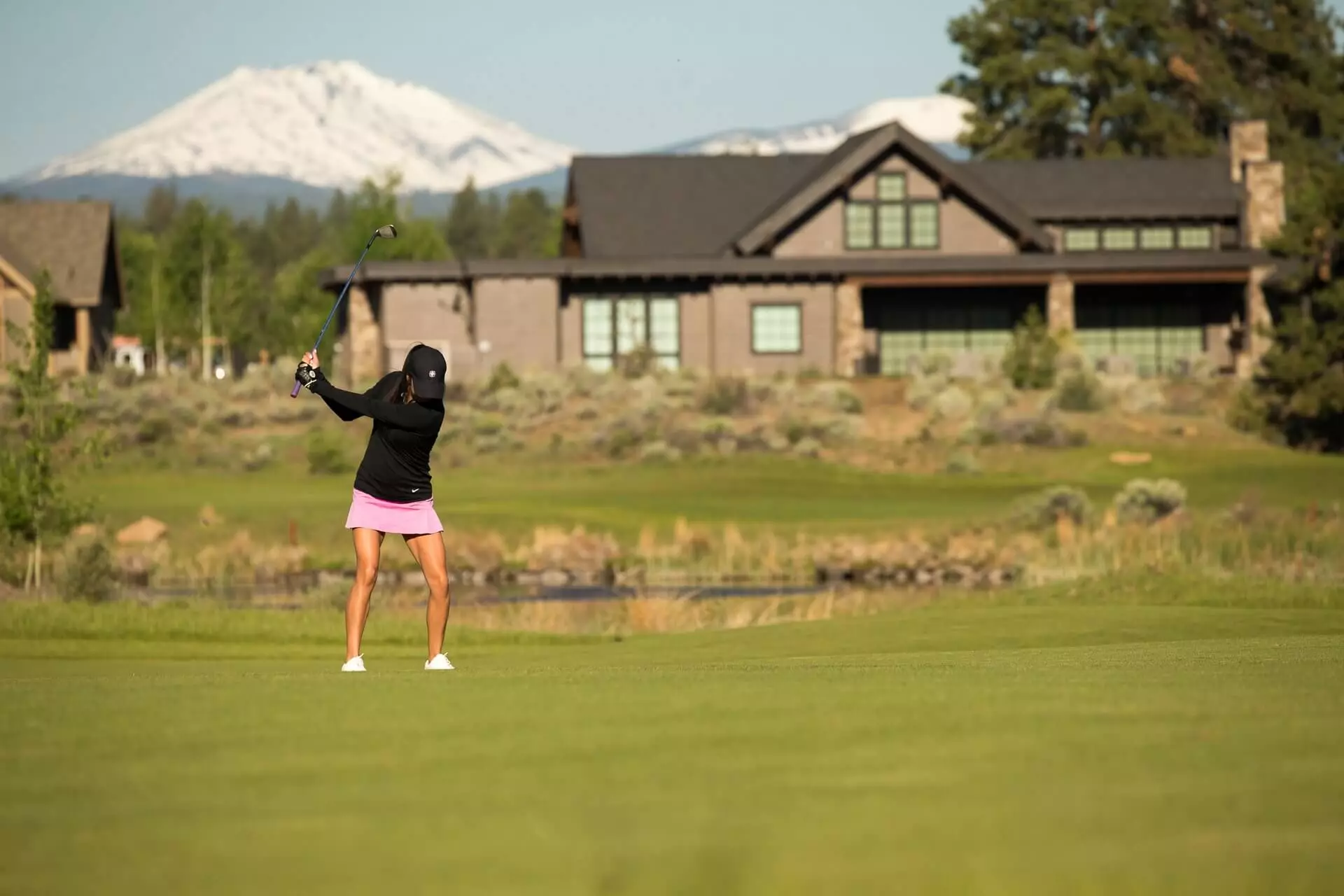 A golfer hits a golf ball in front of a house and mountain views. A golfer hits a golf ball in front of a house and mountain views.